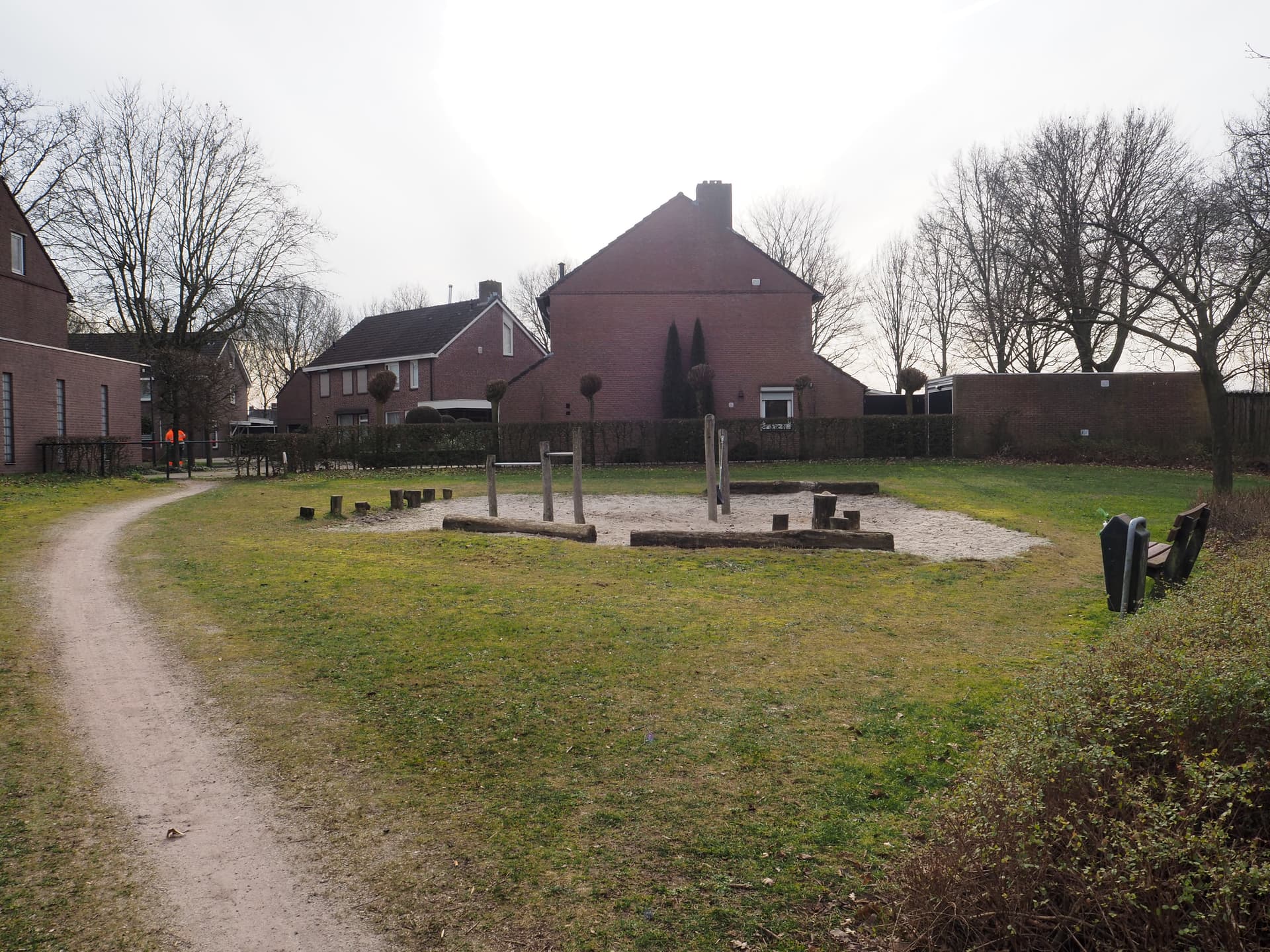 Enlarge image: on the left, a dirt path with a sandbox to its right with tumble bars and tree trunks in it