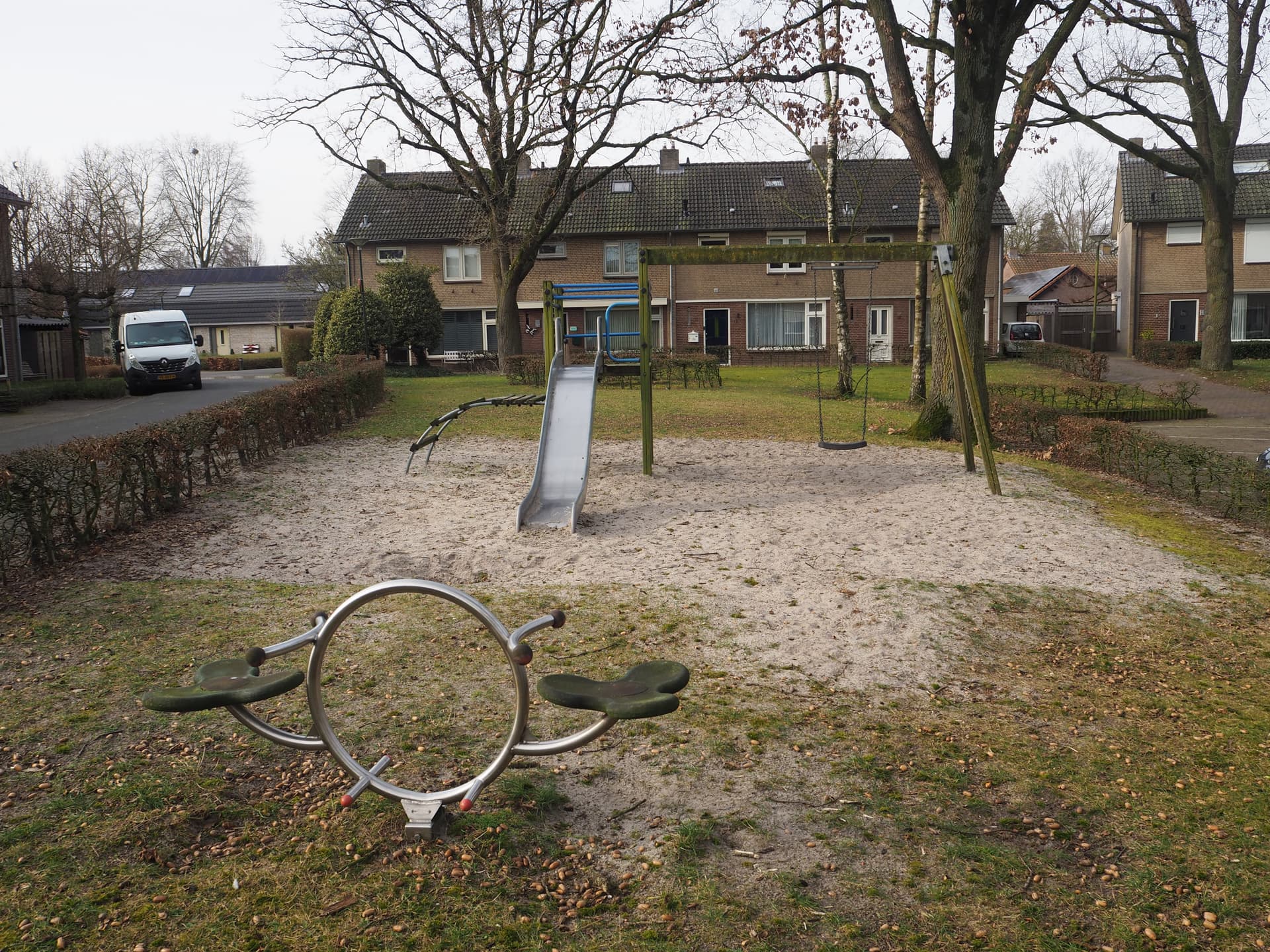 Enlarged image: in front a small seesaw with behind it a climbing frame with slide and swing. In the background are houses.