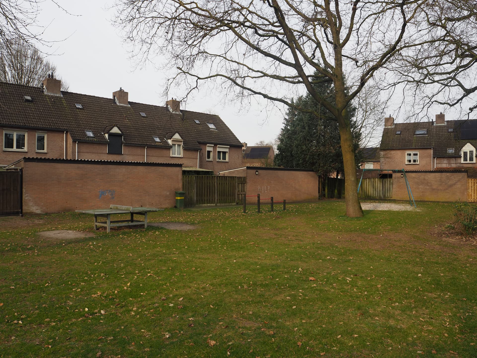 Enlarged image: on the left a table tennis table, to its right a tumble frame and swing. In the background are houses